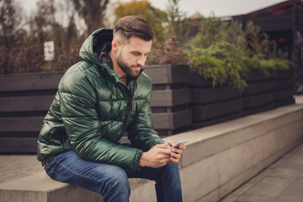 侧面照片英俊迷人的年轻男子穿着绿色风衣打字现代设备城外城市街道图片下载