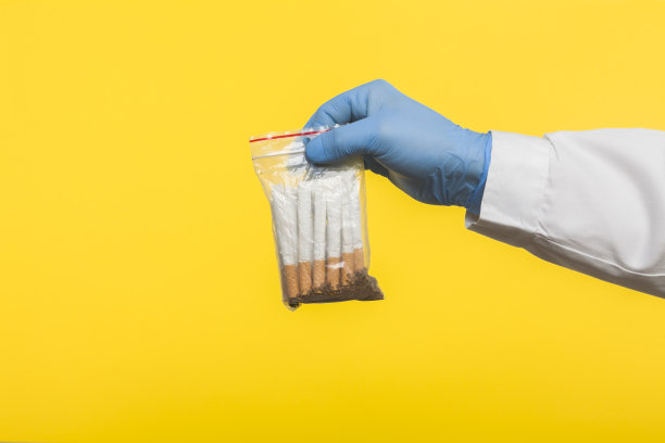 一个戴着防护手套的医生拿着一个密封的铝箔袋，里面装着香烟，黄色的背景被隔离开来图片下载