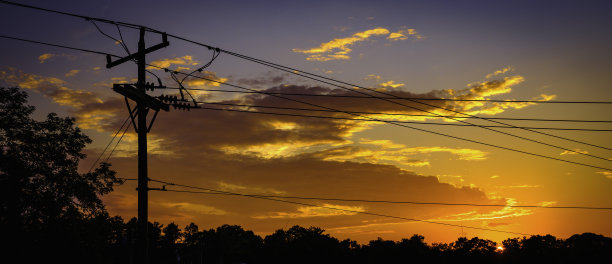 日落时，有引人注目的橙色云彩，电线杆和电缆的剪影图片下载