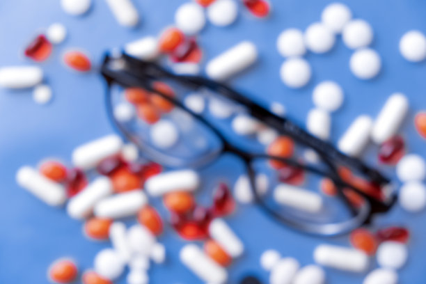 蓝色背景上有一堆不同药丸的眼镜，没有对焦。药物眼治疗概念。视力治疗。医疗、医学。药胶囊药片。图片下载