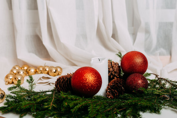 斯堪的纳维亚圣诞贺卡与红色的球在白色的织物背景。里面有白色蜡烛的圣诞花环。绿色的冷杉枝，松果，红色的球和蜡烛在白色的背景与文字的空间。图片下载