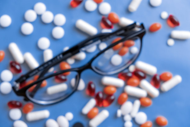 蓝色背景上有一堆不同药丸的眼镜，没有对焦。药物眼治疗概念。视力治疗。医疗、医学。药胶囊药片。图片下载