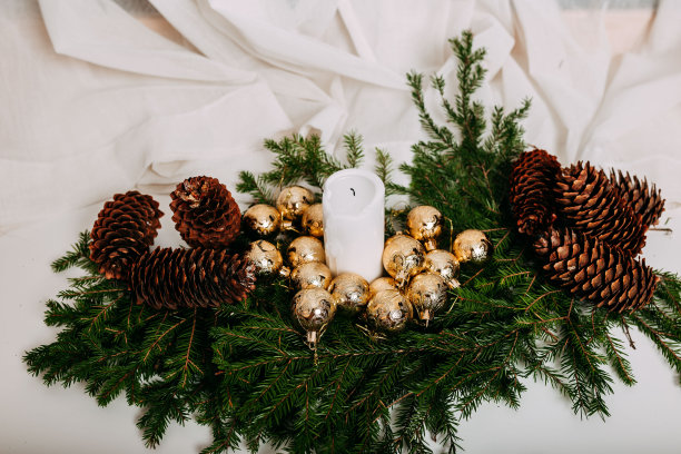 斯堪的纳维亚圣诞贺卡与白色织物和圣诞花环与白色蜡烛内。绿色的冷杉枝，松果，金色的球和蜡烛在白色的背景与文字的空间。图片下载