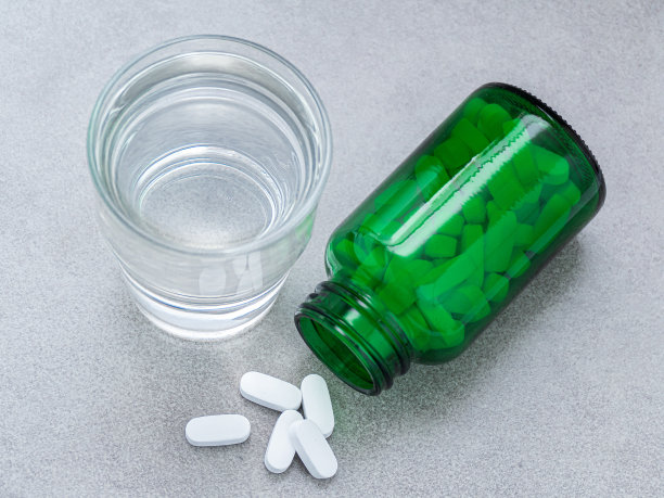瓶子里的药丸，灰色背景和一杯水图片下载