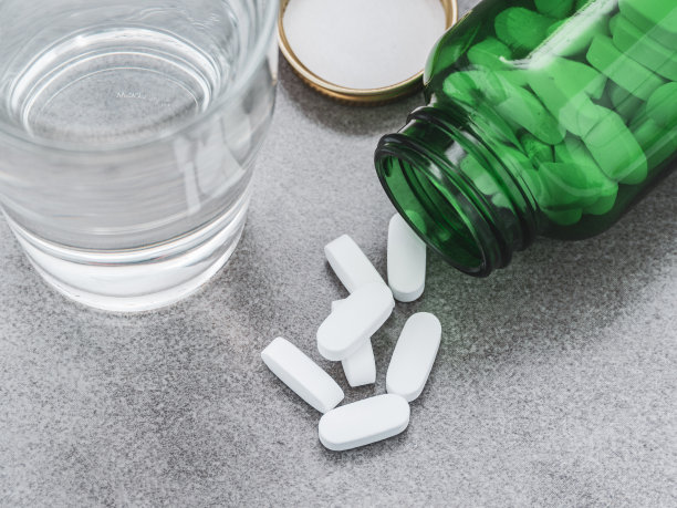 瓶子里的药丸，灰色背景和一杯水图片下载