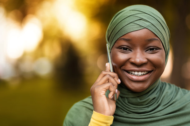 戴着头巾的快乐黑人穆斯林妇女在户外用手机交谈的肖像图片下载