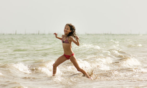 快乐的年轻女孩在海滩上玩耍在浅滩上跑步图片下载