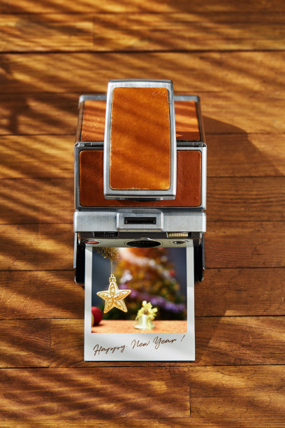 下午的阳光下，木制的桌子上放着一台老式即时胶卷相机和一张印有新年祝福的圣诞装饰品照片。新年的概念图片下载
