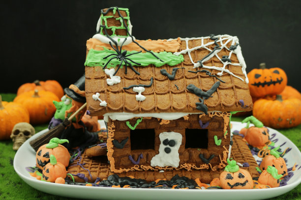 这是自制的万圣节姜饼饼干屋的特写图片，在苔藓的工作台上用糖霜和糖果糖果装饰，南瓜和女巫雕像图片下载