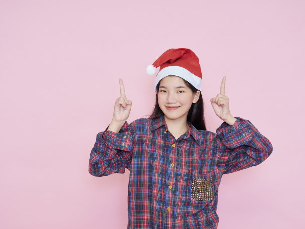 十几岁的女孩在圣诞老人的帽子指着手指空间的文字在粉红色的背景。图片下载