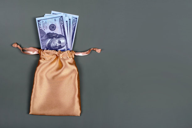 金钱在金色礼品袋灰色背景与copyspace文字。储蓄投资的概念。美元，现金，奖金，奖金，一堆100美元的钞票图片下载