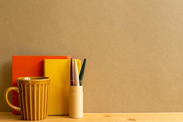 木桌上放着杯子，笔记本，笔。棕色的背景图片下载