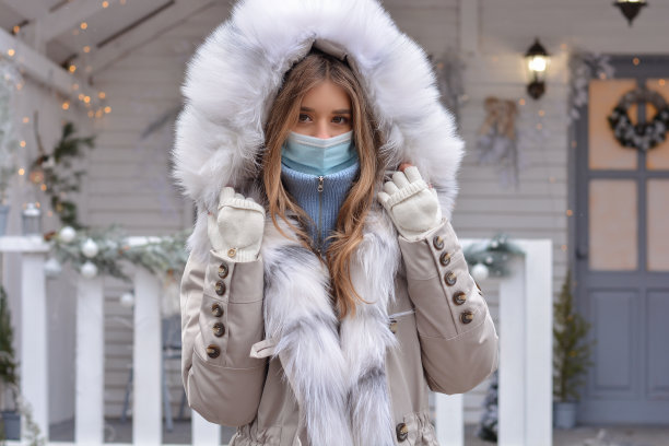 一个漂亮女孩的肖像，穿着大衣，戴着手套，戴着医用面具在圣诞房子的背景上。在新冠肺炎疫情期间，平安度过圣诞节和新年图片下载