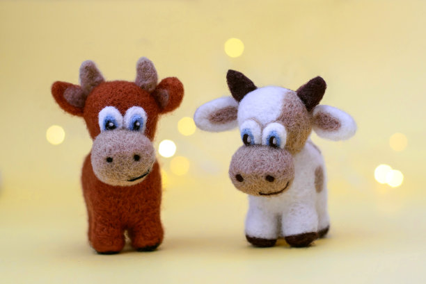 两个毛毡玩具公牛在一个黄色的背景与散焦图片下载