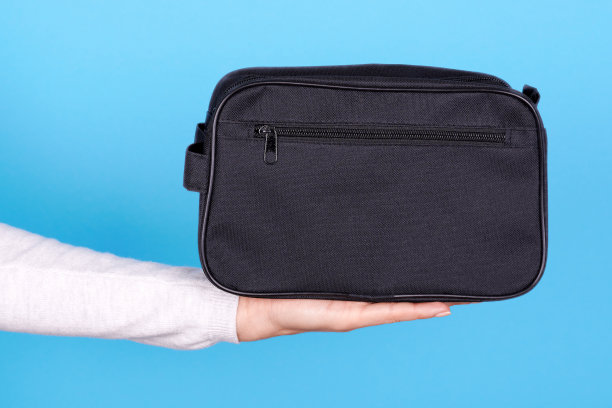手拿黑色化妆包在蓝色的背景。图片下载