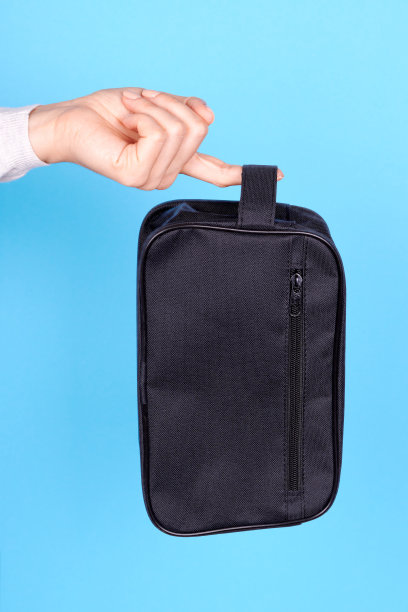 手拿黑色化妆包在蓝色的背景。图片下载