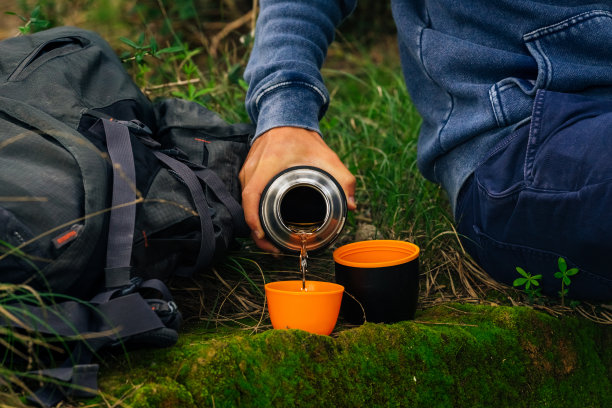 徒步旅行时喝热水瓶里的茶。男人用手从热水瓶里倒热茶图片下载