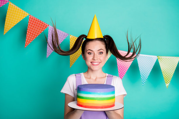 照片肖像的有趣的生日女孩戴帽尾保持彩虹蛋糕微笑孤立在生动的蓝绿色背景图片下载