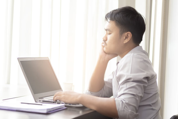 在办公室的木桌上放着笔记本电脑和纸张，亚洲商人感到工作压力很大。亚洲男人在工作不成功时很担心。图片下载