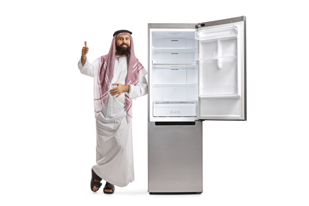 一名苏蒂阿拉伯男子倚靠在空冰箱上竖起大拇指的全长肖像图片下载