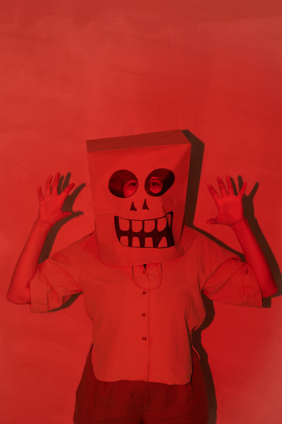 恐怖女人的肖像在万圣节纸袋面具手势，同时在红色的黑暗的房间里吓你图片下载