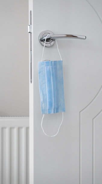 一个面具挂在一个公司大楼的门把手上，特写。提醒大家预防新冠肺炎大流行感染的安全措施图片下载