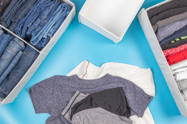 垂直存放衣物，整理房间，打扫房间的概念。把折叠好的t恤和牛仔裤堆放在篮子里，还有一堆没拿的衣服。俯视图图片下载