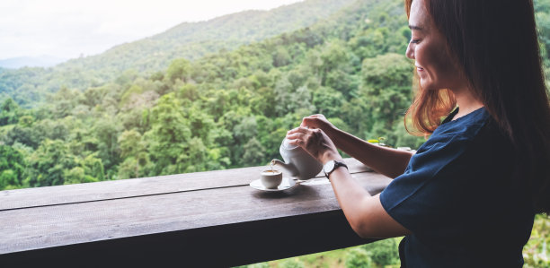 一位亚洲妇女把茶倒进木桌上的一只白色杯子里图片下载