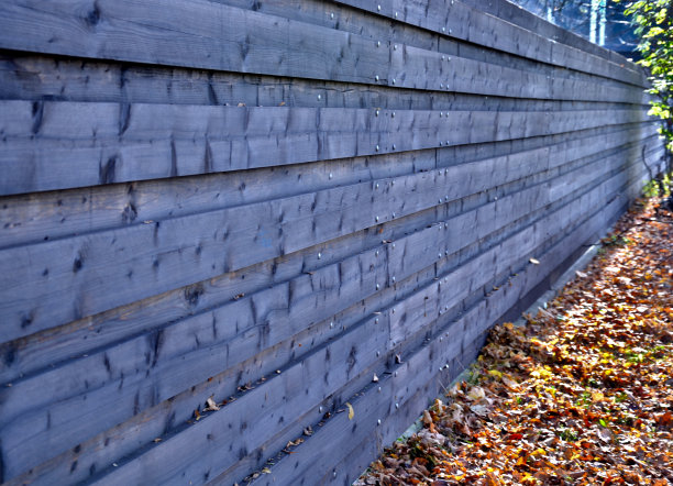 不透明的棕色木制栅栏，水平附着木板。在街上行驶的汽车发出噪音时，用栅栏来防止。秋天的叶子可以采摘或用割草机覆盖图片下载