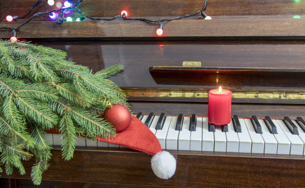 新年的室内装饰有蜡烛、灯泡和圣诞树。这架钢琴是为了庆祝圣诞节而装饰的。钢琴键。有选择性的重点。图片下载