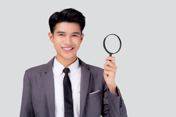 年轻的亚洲商人西装看着放大镜搜索孤立的白色背景，商人的表情和发现质量，检查员和审查，男性的表情。图片下载