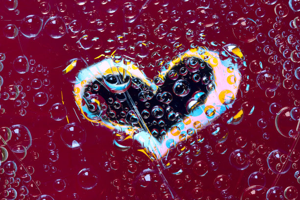 多颜色的水滴位于一个紫红色-黑色的背景与蓝-黄-粉红色的心剪影。图片下载