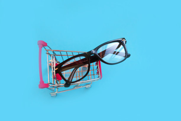 儿童眼镜在一个黑色的塑料框架在一个小的购物车在蓝色的背景，复制空间，特别防破坏儿童眼镜框架。图片下载