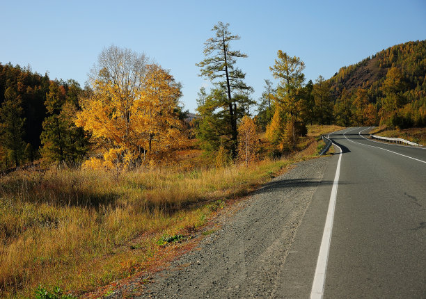 一条双车道的柏油路蜿蜒在秋天的山谷里的群山之间。图片下载
