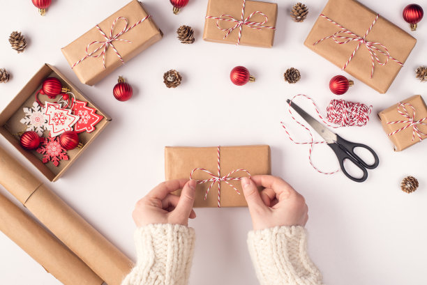 圣诞快乐的概念。Top flatlay近距离俯瞰女性双手包裹礼物的照片在白色的桌子上素材图片