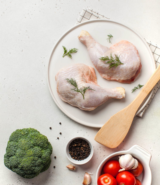 养殖家禽。冷冻生鸡腿与蔬菜和香料放在盘子里。副本的空间。图片下载