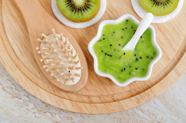 新鲜的猕猴桃泥在一个小的白色碗和木制发刷。自制护发或面膜，天然美容及水疗配方。俯视图，复制空间。图片下载