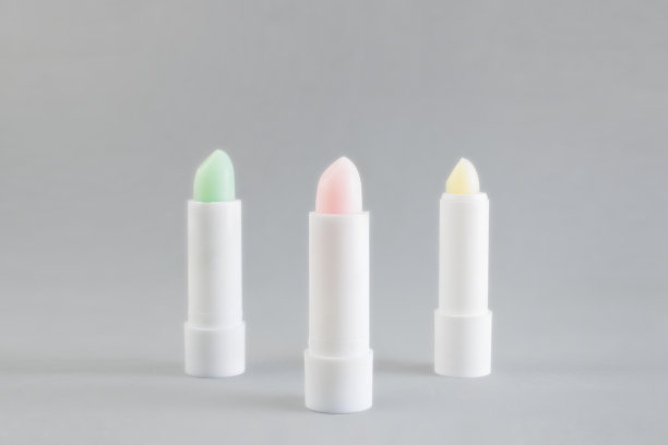 白色管粉色，绿色和黄色唇膏保护和滋养嘴唇在灰色的背景。冬季化妆品。容器的布局。给女人的礼物。本空间图片下载