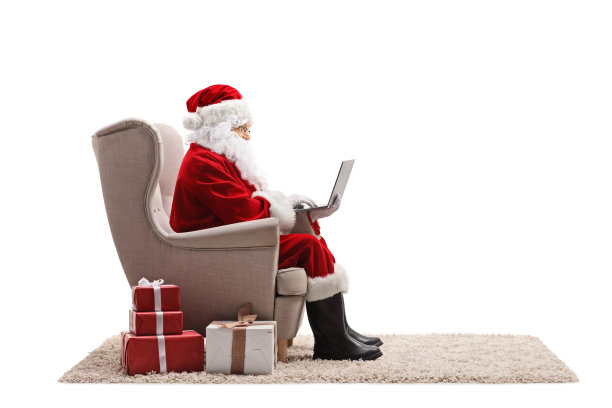 圣诞老人在笔记本电脑上工作，坐在扶手椅上，礼物放在地板上，在白色的背景上孤立图片下载