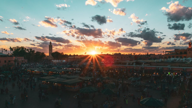 日落时分，亚马埃尔夫纳广场上有集市和人群，背景是清真寺塔。旅行的概念。摩洛哥马拉喀什图片下载