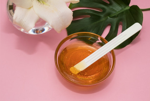 蜜糖脱毛膏在碗与百合和龙血草叶玻璃花瓶在粉红色的背景，身体护理图片下载