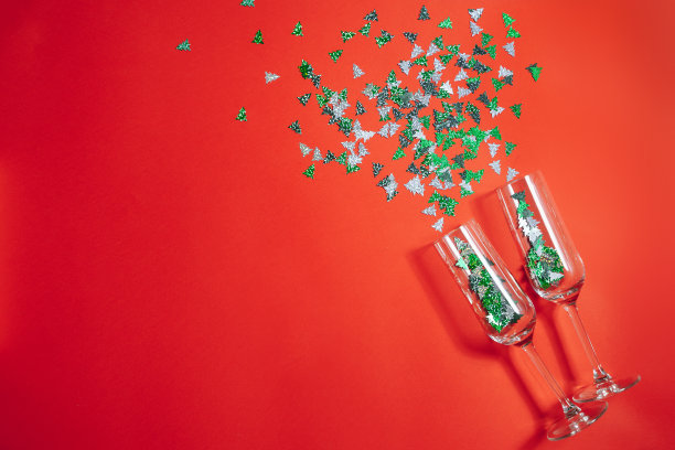 红色背景上的两个香槟杯，五彩纸屑飞溅成圣诞树的形状。新年和圣诞节的概念。图片下载