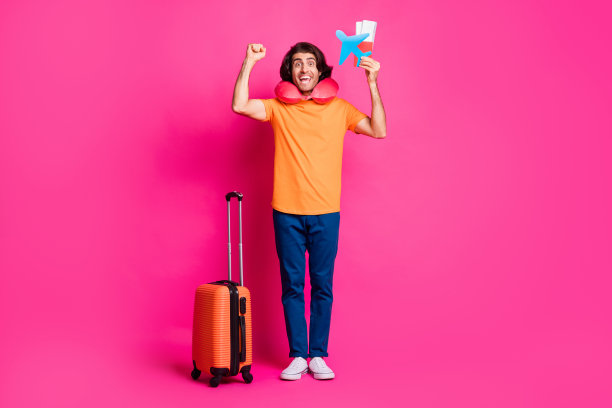 全长照片的家伙行李票纸飞机举起拳头穿颈部坐垫橙色t恤牛仔裤运动鞋孤立亮粉色背景图片下载