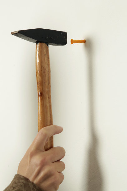 年轻女子正在往墙上钉钉子。家居装修，DIY概念。图片下载