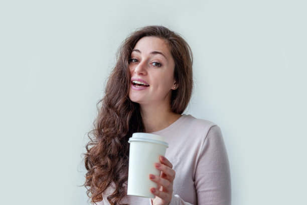 美丽年轻的黑发女人与带走的纸咖啡杯孤立在白色的背景。快乐微笑的女孩正在吃午饭。早上喝饮料休息休闲的概念图片下载