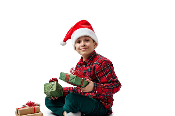 一个孩子在白色上的孤立肖像。一个穿着红色衬衫的男孩坐在那里微笑着，手里拿着圣诞礼物。图片下载