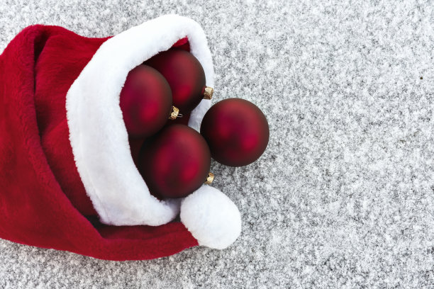 红色白色的圣诞背景。毛茸茸的圣诞老人帽子上挂着红色的圣诞球，上着白霜，下着雪。冬天假日季节。圣诞快乐，恭贺新禧。图片下载