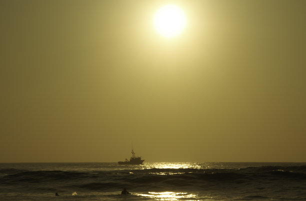 海滩上的日落与冲浪者和一艘船的背景。图片下载