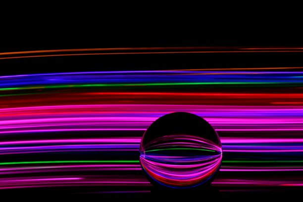 长时间曝光的霓虹灯照片，在一个抽象的漩涡，平行的线条模式与黑色的背景反射在一个玻璃球球。光绘摄影。图片下载