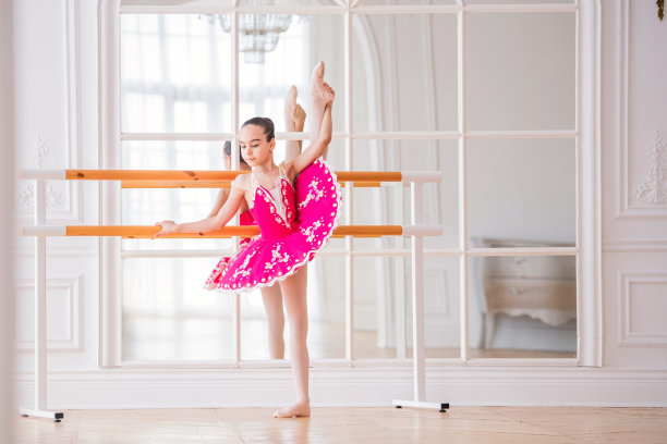 在一个美丽的白色大厅里，一个穿着亮粉色芭蕾舞裙的小芭蕾舞演员在一面镜子前跳芭蕾舞图片下载